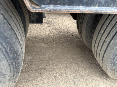 Trailer frame showing dual heavy-duty rear axles with large tires on a Load King lowboy. Dust on tires and ground visible.