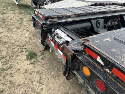 Lowboy trailer rear corner showing hydraulic lines and control box, Load King branding not visible, weathered black frame with red and white reflective tape.