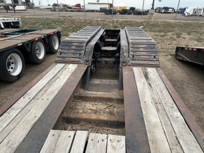 Lowboy trailer deck and kingpin area showing weathered steel rails and wooden planks on a Load King RGn lowboy.