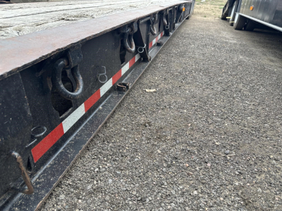 Lowboy trailer edge showing hooks and reflective red/white stripe along the side, from a ground-level view.