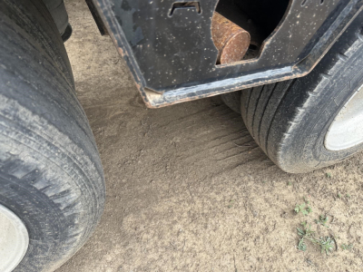 Lowboy trailer wheel area showing dual tires and frame with visible dirt and grounding surface.