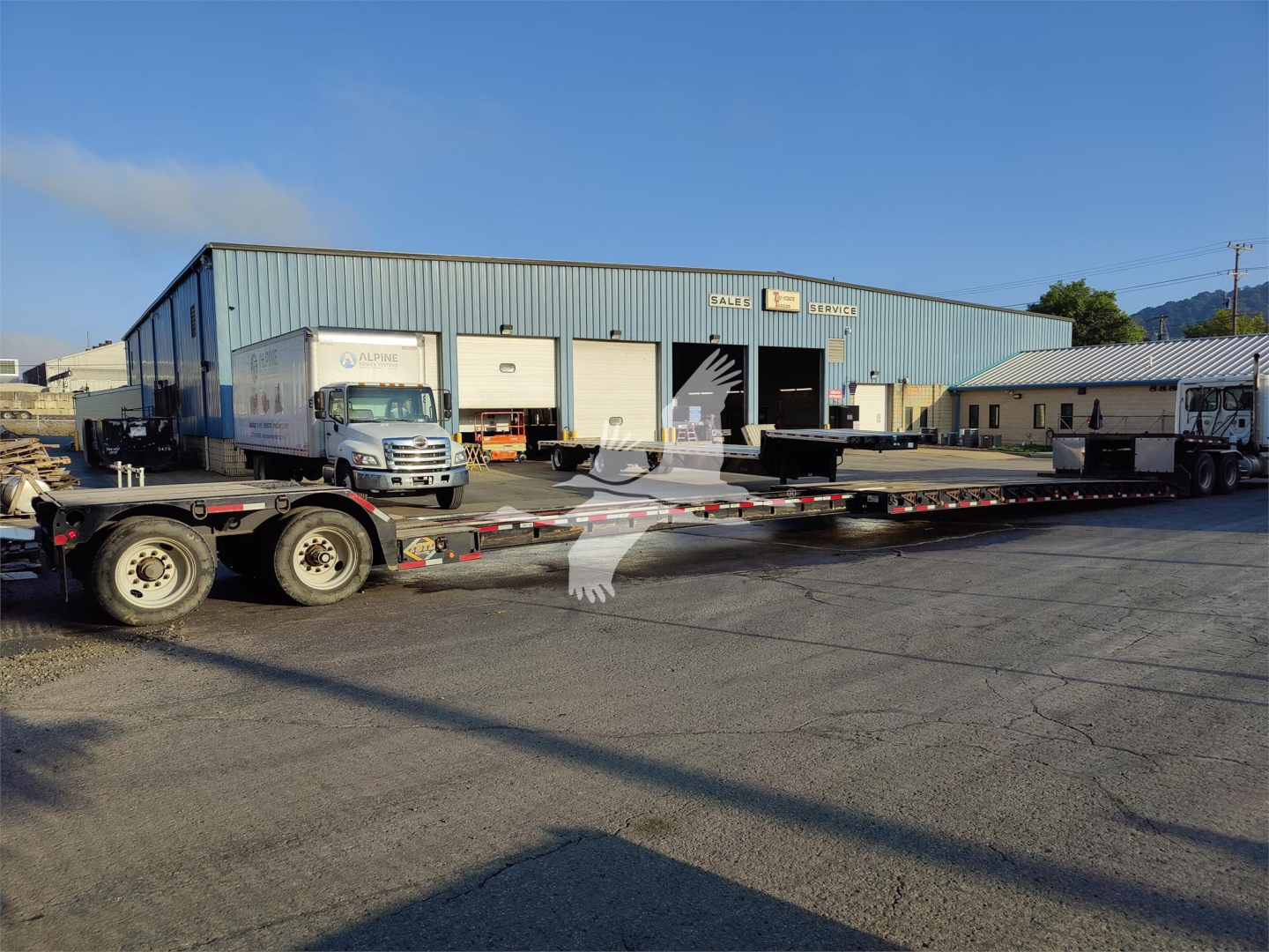 Fontaine Renegade Lxt-40 trailer in a yard with a flatbed and loading dock doors visible.