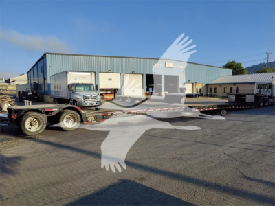 Trailer parked outside a blue warehouse with a Fontaine LXT-40 double drop expandable trailer on a flatbed truck, stock number 53-5975, VIN 57J653206L3577453.