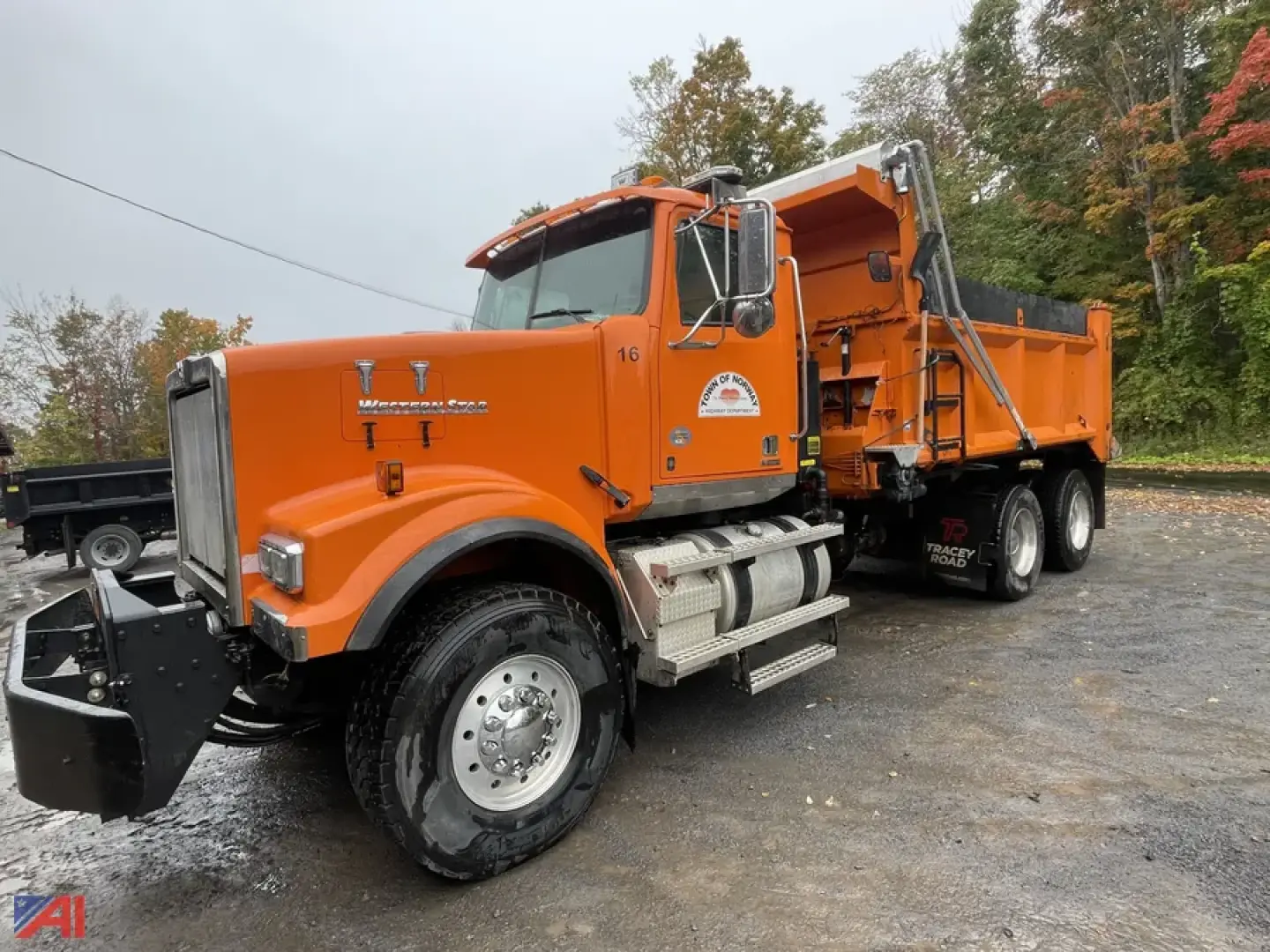 Dump truck showing orange Western Star 4900 SF with plow and dump body, side view with front bumper and wheel rims visible.
