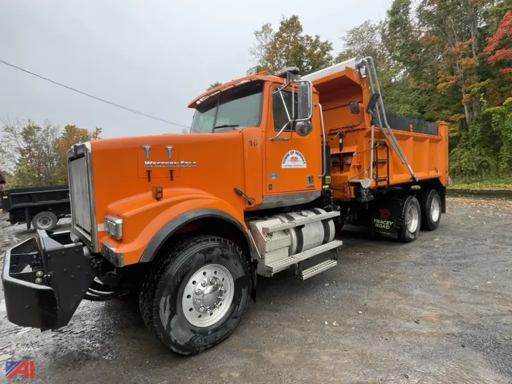 Dump truck showing orange Western Star 4900 SF with plow and dump body, side view with front bumper and wheel rims visible.