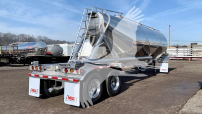 Heil Cementer pneumatic dry bulk trailer with stainless steel cylindrical tank and dual rear axles in a dealership lot.