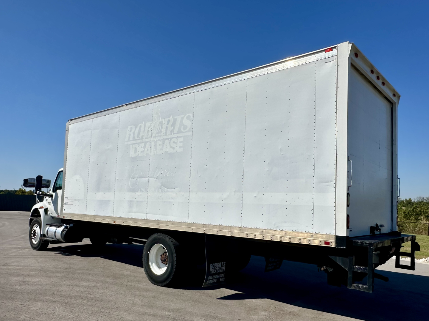 Box truck side view showing RockParts Dealase faded logo on a silver cargo box and rear cap, International MV607 in a parking lot.