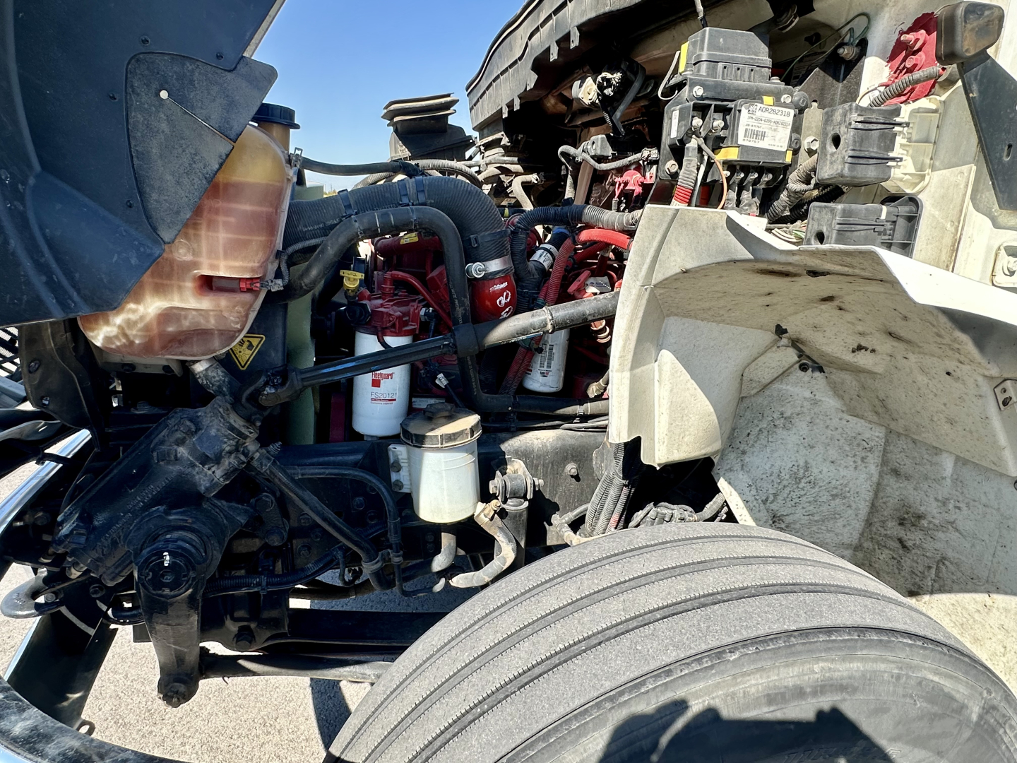 International MV607 engine bay showing coolant reservoir, filter, hoses, and wiring. Visible components include coolant bottle, oil filter, air intake hoses, and battery area.