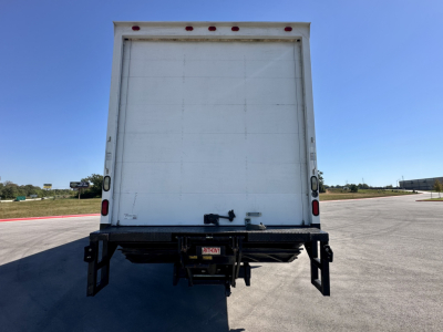 Back view of a white box truck cargo area with rear doors closed; hitch and bumper visible, empty road and clear sky in background.