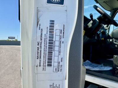 Vehicle side door sticker with VIN and bar code label on left door pillar of 2023 International MV607 truck, interior visible through open cab, sticker has vertical text and barcode.