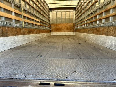 Truck cargo area: empty box truck interior with wooden side walls and metal flooring, seen from rear doorway.