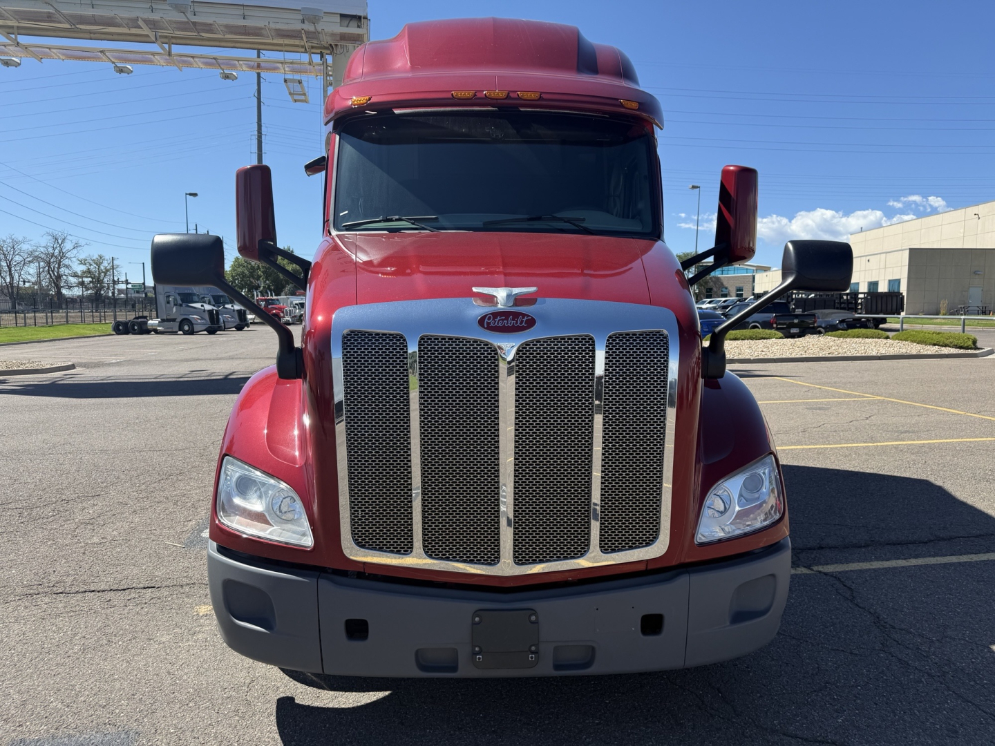 Peterbilt 579 front view showing grille, hood, headlights, and bumper. Red paint with black lower fascia and large chrome grille.
