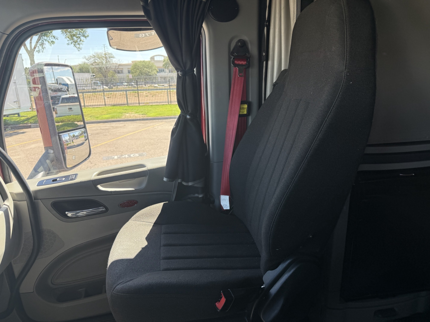 Peterbilt 579 truck interior view with driver seat and door panel, seatbelt visible, side mirror and window in background.
