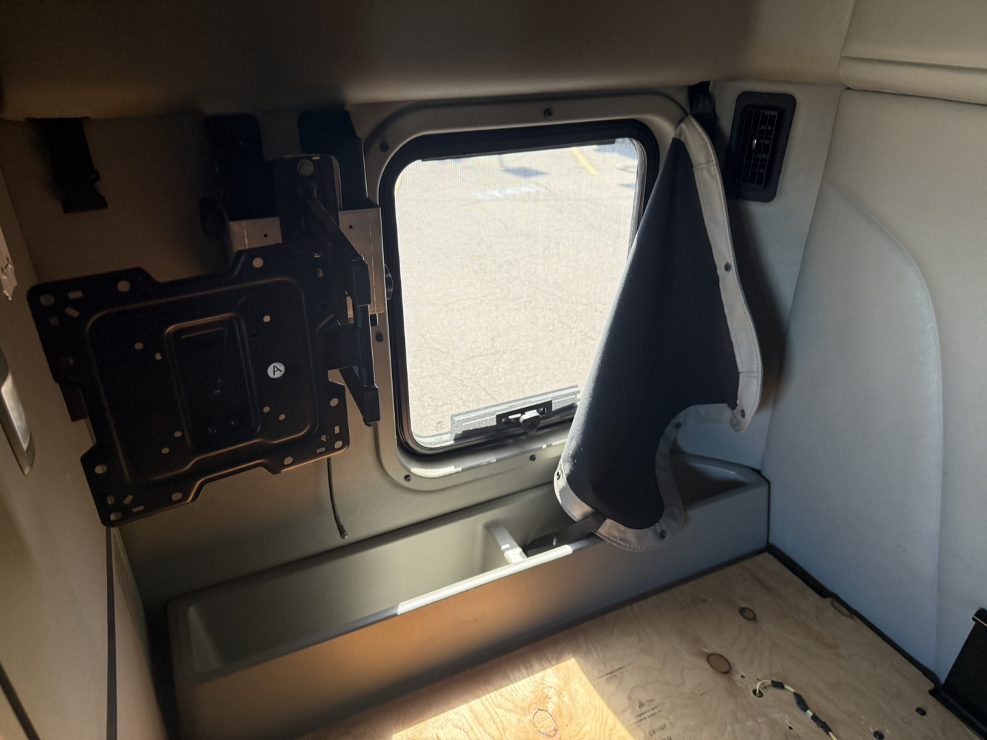 Cab interior with side window opening and mounting bracket in view. Includes a wall panel, window, and floor surface.