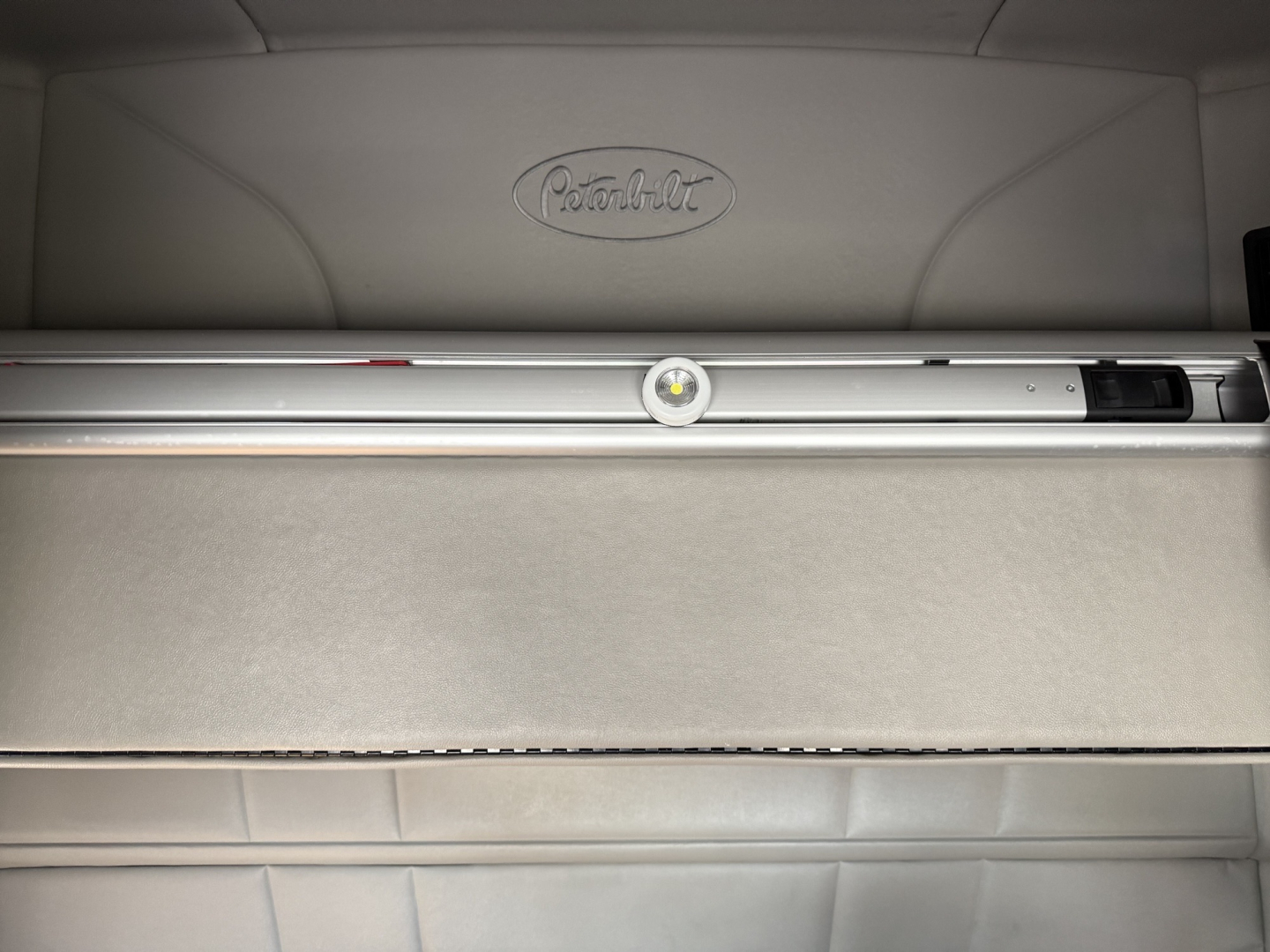 Peterbilt logo on a sleeper cab interior with a horizontal storage drawer and metal rails