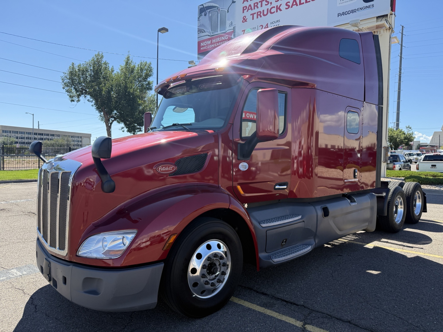 Peterbilt 579 sleeper cab tractor in maroon showing front grille and wheel well, side view with windows and mirrors.
