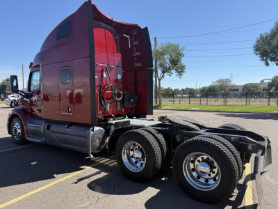 Peterbilt 579 conventional sleeper truck rear view showing dual rear axles and fifth wheel for hitch, red cab, chrome fuel tanks, and wheel rims.