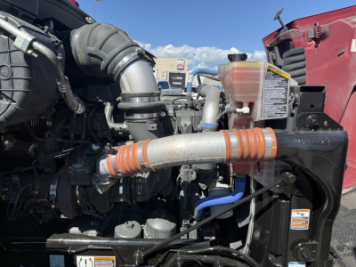 Peterbilt engine bay with intake tube, coolant reservoir, and hoses visible; label on reservoir and warning stickers on radiator support.