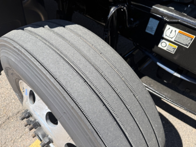 Peterbilt 579 truck wheel/tire close-up showing single tread with metal wheel and lug nuts; part of truck undercarriage visible.