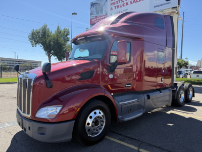 Peterbilt 579 sleeper cab tractor in maroon showing front grille and wheel well, side view with windows and mirrors.