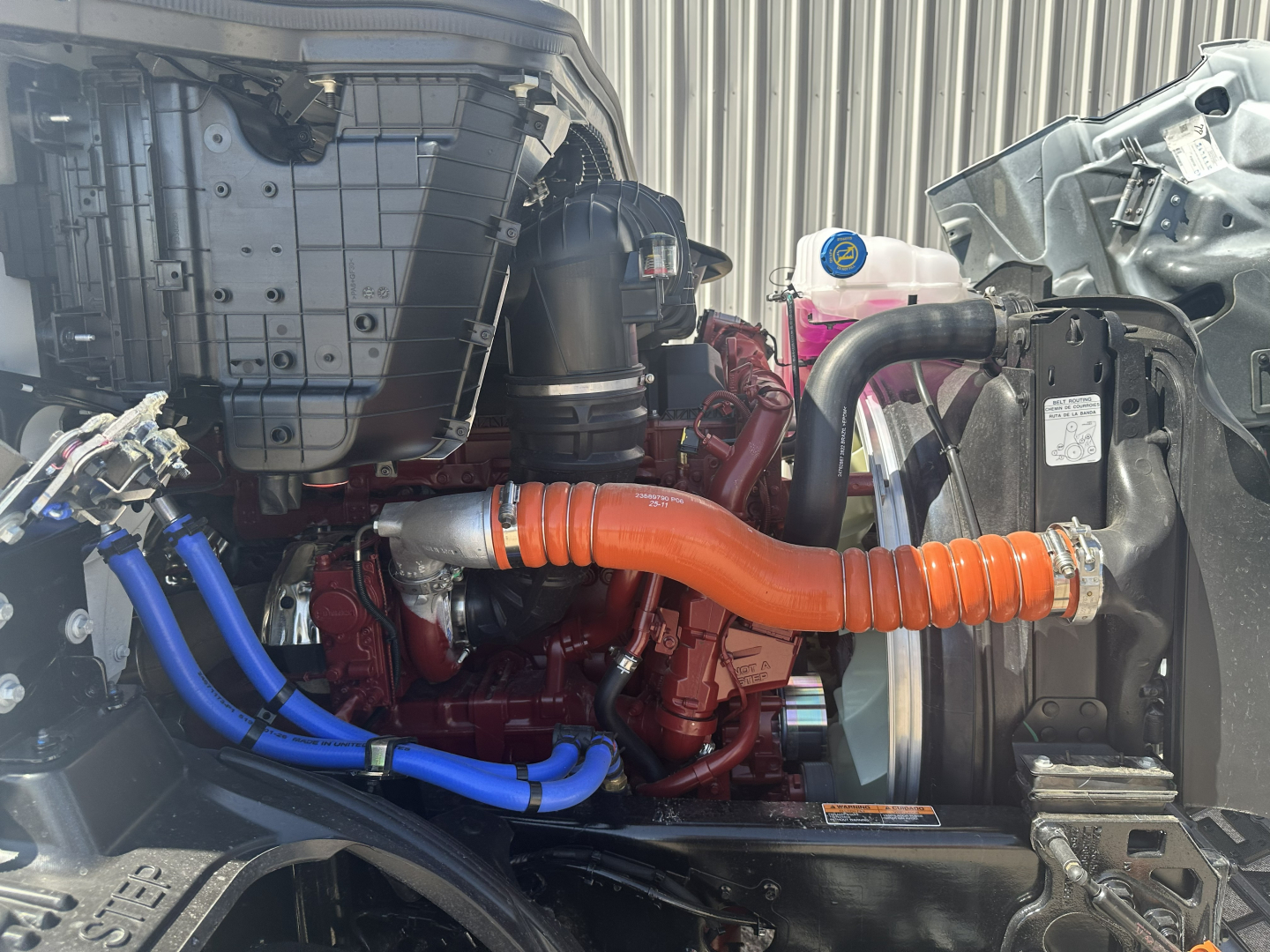 Mack AN64T engine bay showing orange flexible intake tube and blue hoses connected to turbo and coolant system.
