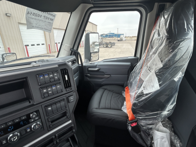 Cabin interior of a 2027 Mack AN64T truck showing driver seat and dashboard with wrapped passenger seat.