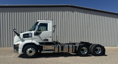 Truck side view showing cab and chassis of a new Mack AN64T conventional daycab with triple axle rear, white cab, black undercarriage.
