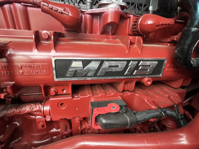 Close-up of a red Mack MP8 engine badge with surrounding engine components.
