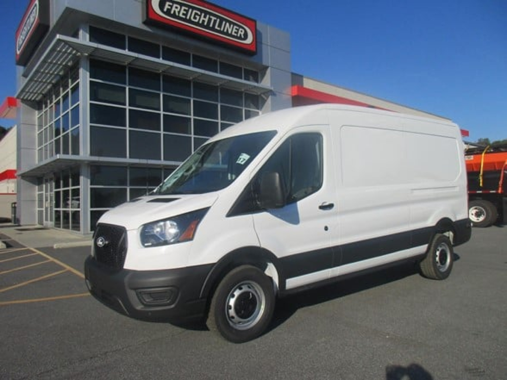 Ford Transit cargo van in front of dealership showing white cargo van with black front bumper and grille, side mirrors, and grey dealership building.