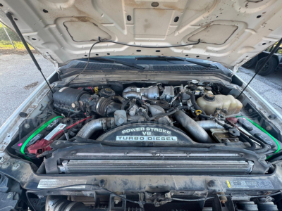 Ford F-550 engine bay with hood open showing turbo diesel power; visible components include air intake, turbocharger, alternator, coolant reservoir, and radiator support plate; text on engine cover reads 'POWER STROKE V8 TURBO DIESEL'