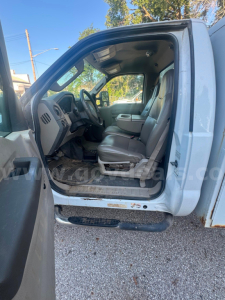 Truck cab interior of a 2008 Ford F550 with open driver door; visible dashboard, steering wheel, and front seats; floor mat; side step; weathered exterior paint.
