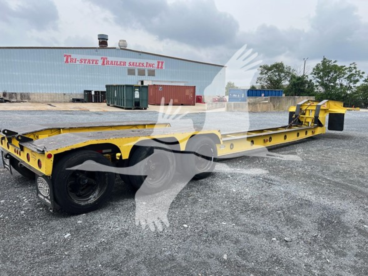 Rogers 50 Ton beam trailer in yellow, long flatbed with rear axles and gooseneck, side rails, trailer hitch area, industrial yard with building in background.