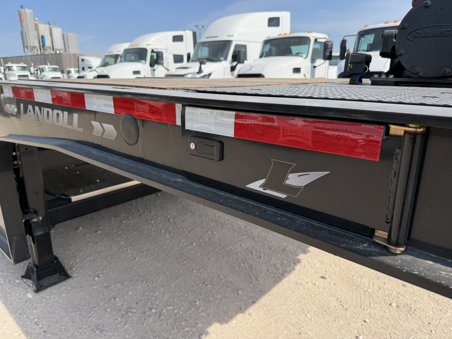 Landoll trailer rear side showing reflective red/white stripe and Landoll logo, lowboy trailer deck, and side panel with stamped metal finish.