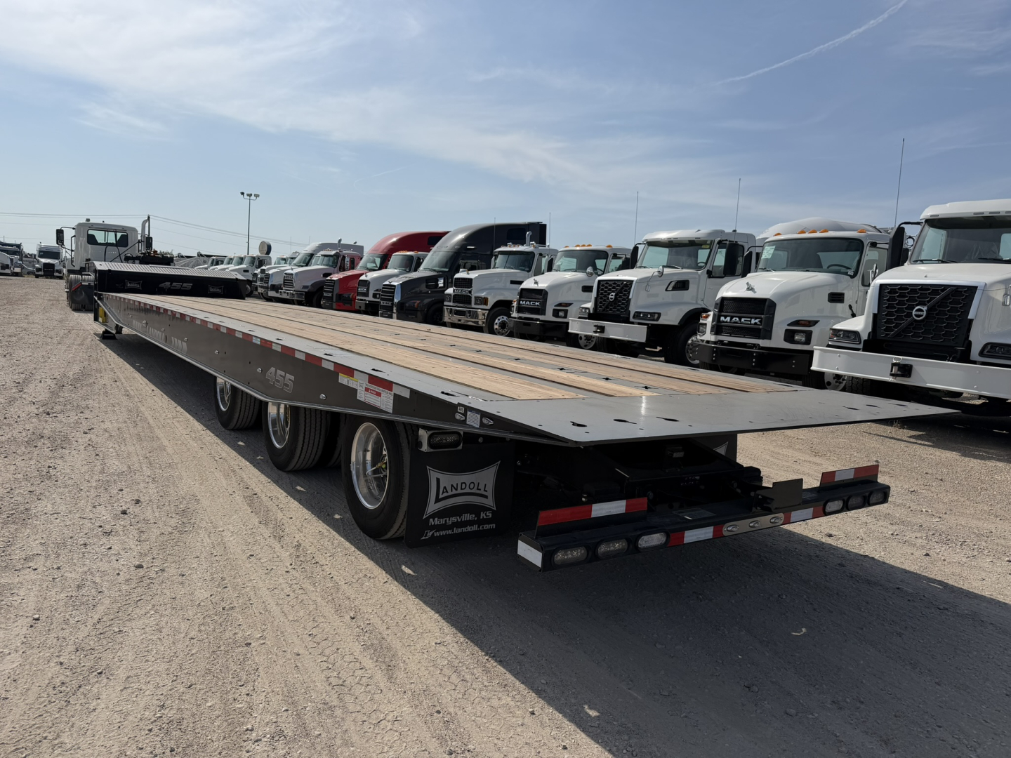 Lowboy trailer in a dealership lot showing long flatbed with dual rear axles and Landoll branding on mudflaps.