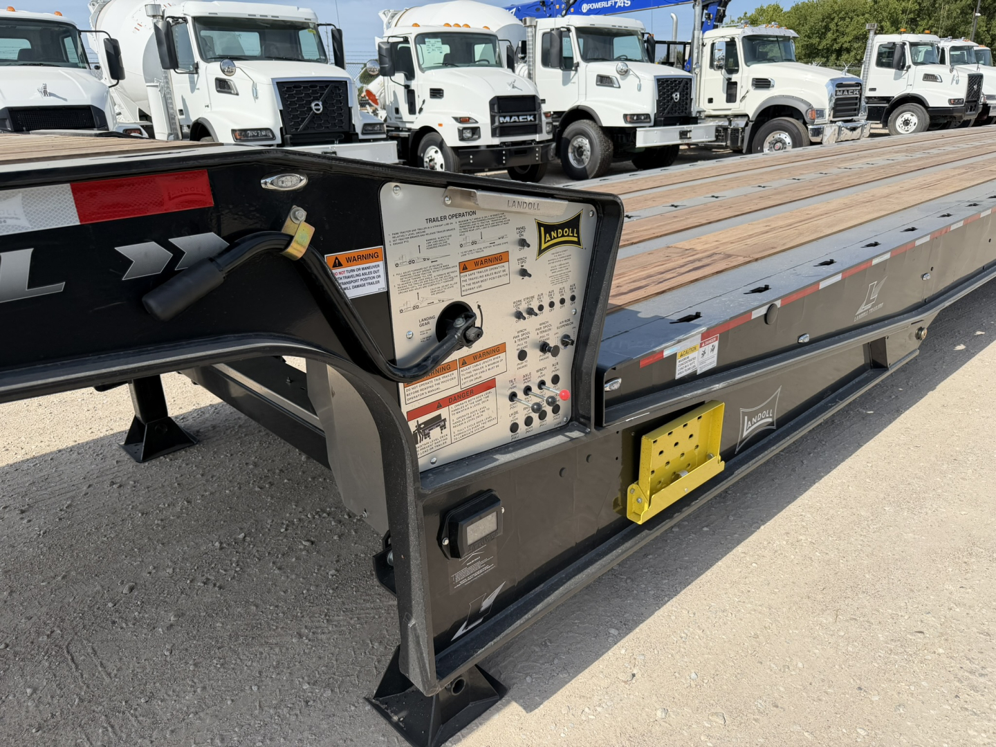 Landoll 455B-53 55 Ton traveling axle lowboy trailer side view showing control plate with labels and warning decals, wooden deck stretch, and yellow jack/attachment points.