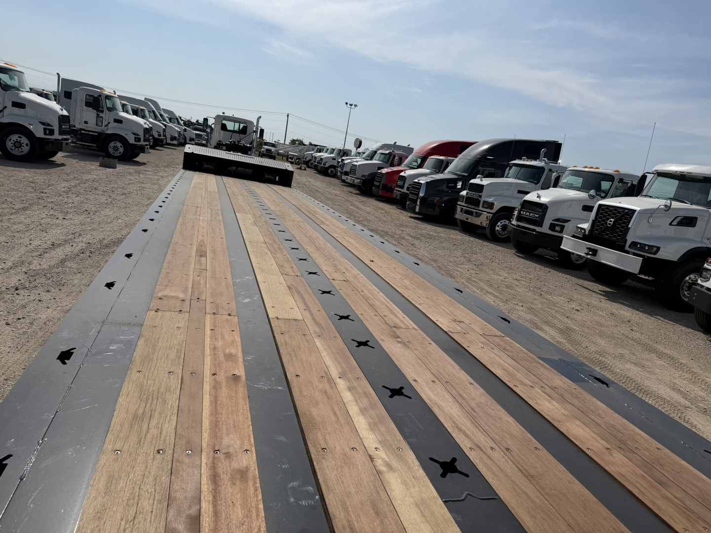 Landoll 455B-53 lowboy trailer bed with wooden planks and steel side rails, showing long deck and multiple trucks in the background.