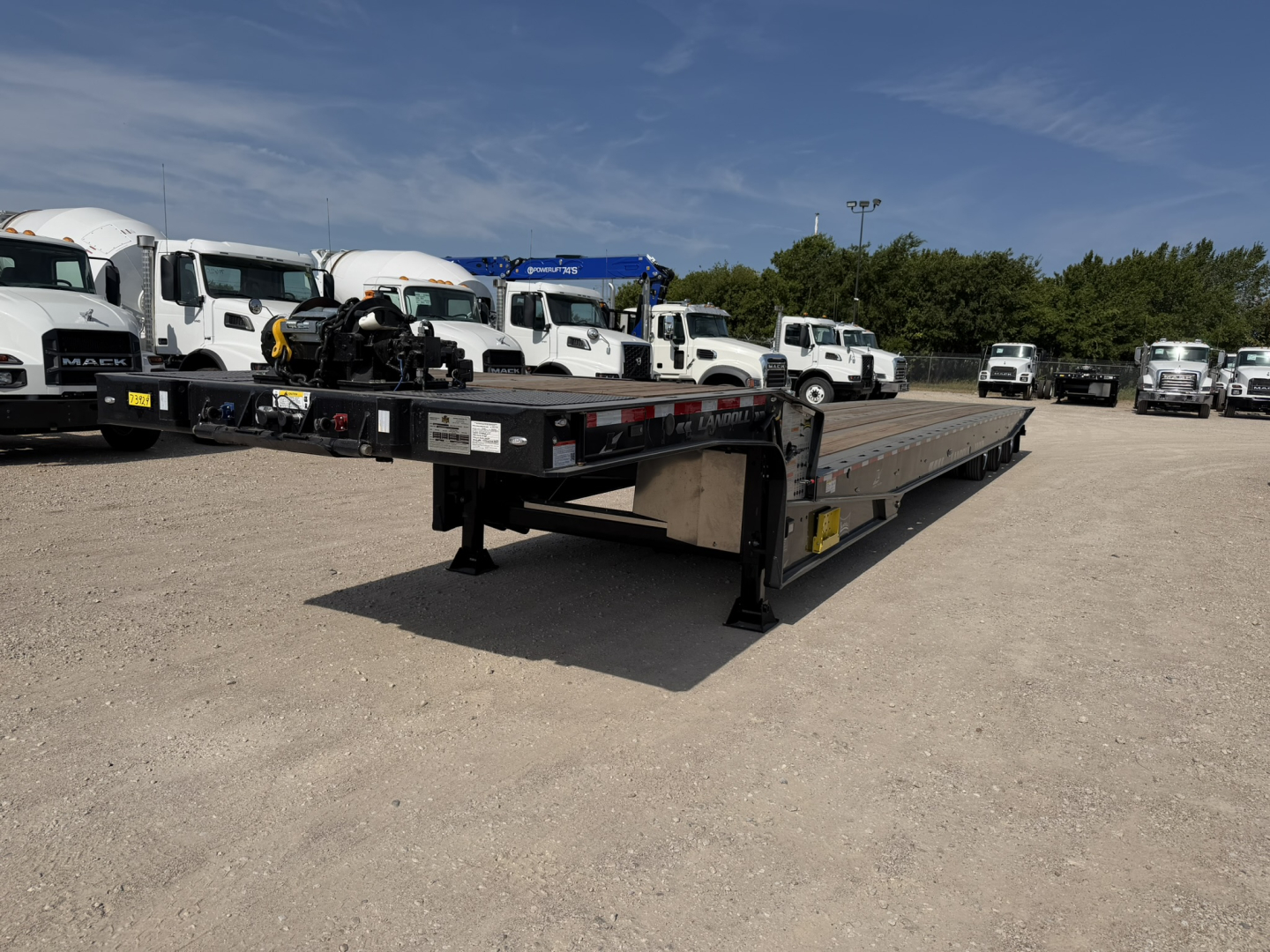 Lowboy trailer showing 55 ton traveling axle with long flatbed and front gooseneck area; visible labels and wheel bunks at rear.