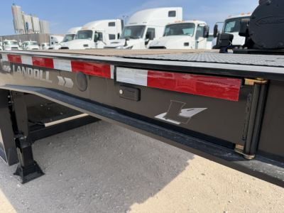 Landoll trailer rear side showing reflective red/white stripe and Landoll logo, lowboy trailer deck, and side panel with stamped metal finish.
