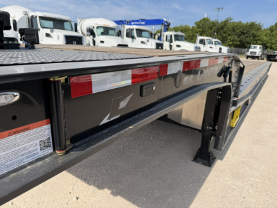 Landoll 55-ton traveling axle lowboy trailer side view showing black steel frame, reflective red/white tape, warning label, and stepped deck.