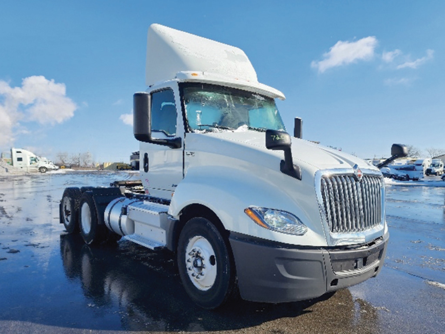 Truck cab and chassis showing 2019 International LT625 daytime running lights and large grille in white, side mirrors, dual rear axles, on a wet lot.