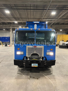 Front view of a blue 2011 Peterbilt 320 truck in a warehouse, Wayne equipment, with a large grille and front bumper.