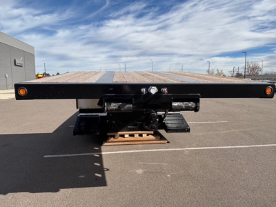 Trailer rear view showing lowboy with wood deck and swingouts, black frame, dual kingpin mechanism, and marker lights.
