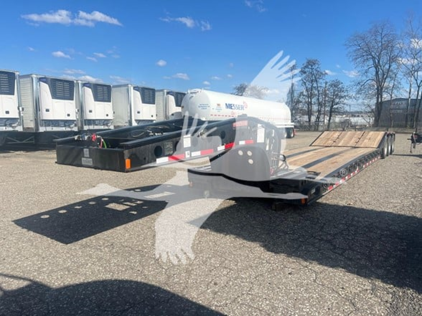 Fontaine paver trailer in a lot, lowboy configuration, with a white hydraulic unit on the deck and multiple trailers in background.