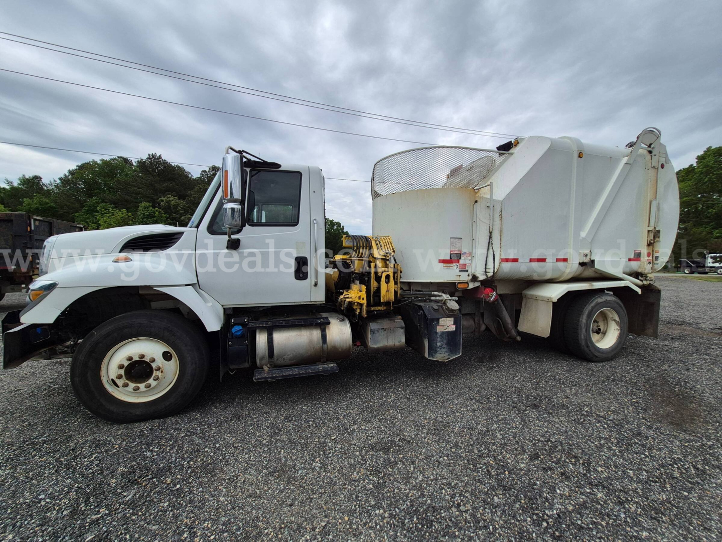 Big white International 7400 dump truck side view with front cab and rear dump body, VIN tag area not visible, street gravel lot.