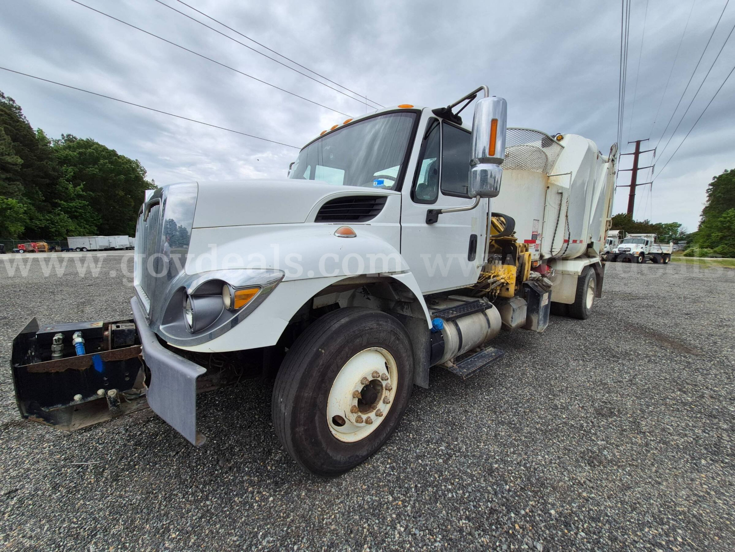International 7400 straight truck with mounted vacuum/garbage body in a gravel lot, side view showing front bumper, dual rear wheels, and hydraulic components.