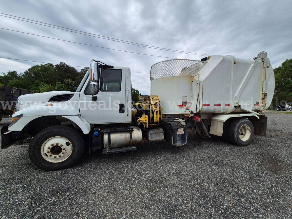 Big white International 7400 dump truck side view with front cab and rear dump body, VIN tag area not visible, street gravel lot.