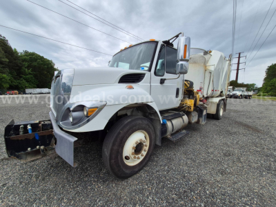 International 7400 straight truck with mounted vacuum/garbage body in a gravel lot, side view showing front bumper, dual rear wheels, and hydraulic components.