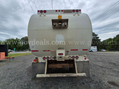 Back view of a white International 7400 trash truck tank showing rear lights and bumper with various small labels and a metal ladder/step structure.
