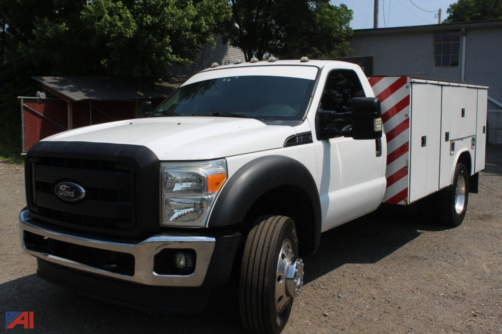 Ford F-550 Super Duty utility truck with service body, front grille and headlights visible, cab white, utility compartments to rear, red-and-white striped panels on the sides.