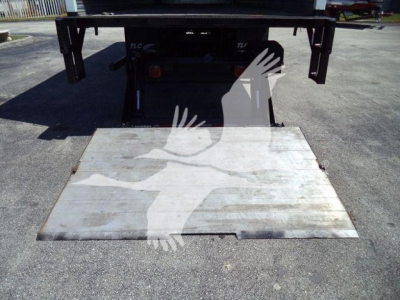 Rear view of a Freightliner M2 106 flatbed truck with a lowered hydraulic lift and metal ramp.